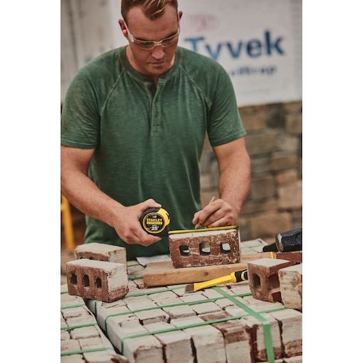 25 foot FATMAX classic tape measure being used by a person to measure brick length.
