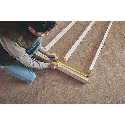 25 foot FATMAX classic tape measure being used by a person to measure wood length.